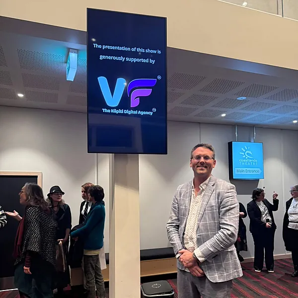 Oli Corby at Coastlands Theatre beneath a screen crediting VF Digital as supporter of the show